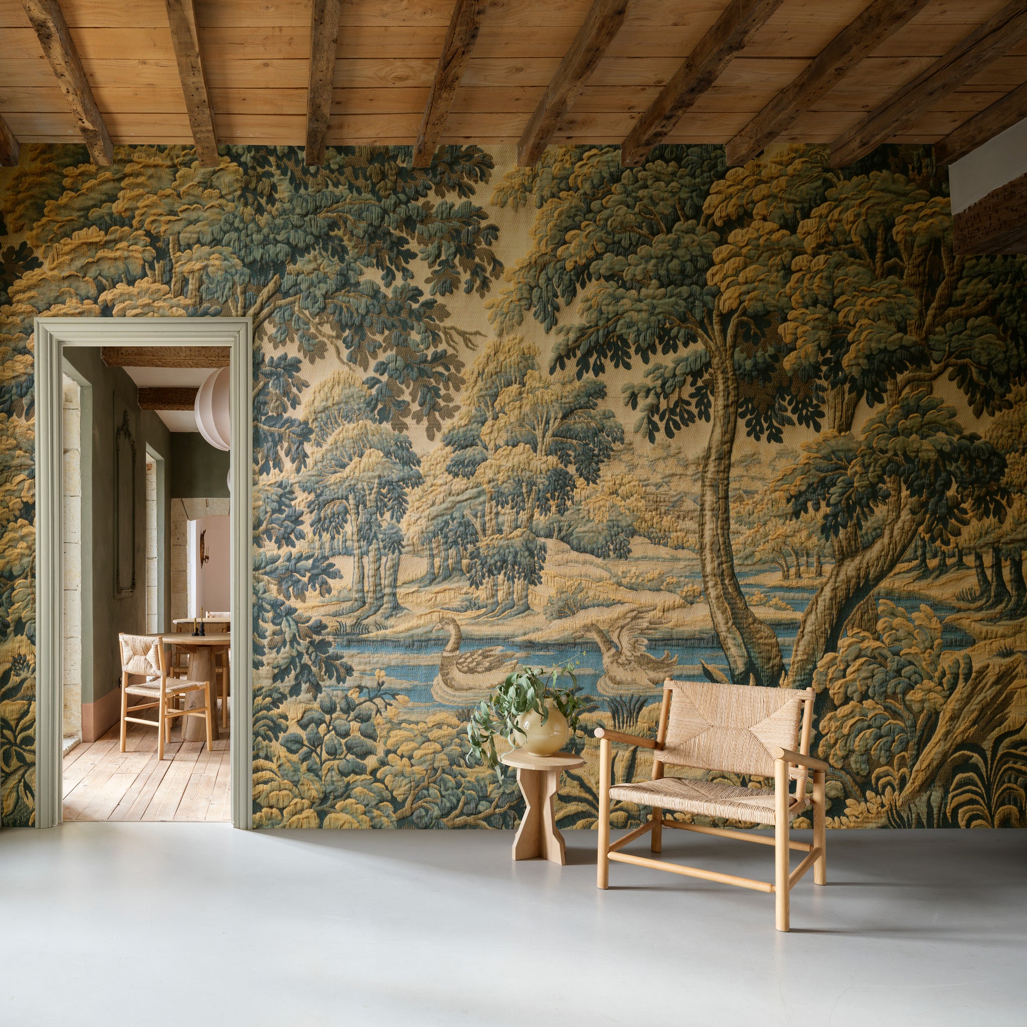Room with tapestry wall featuring a landscape scene, wooden chair, and table.
