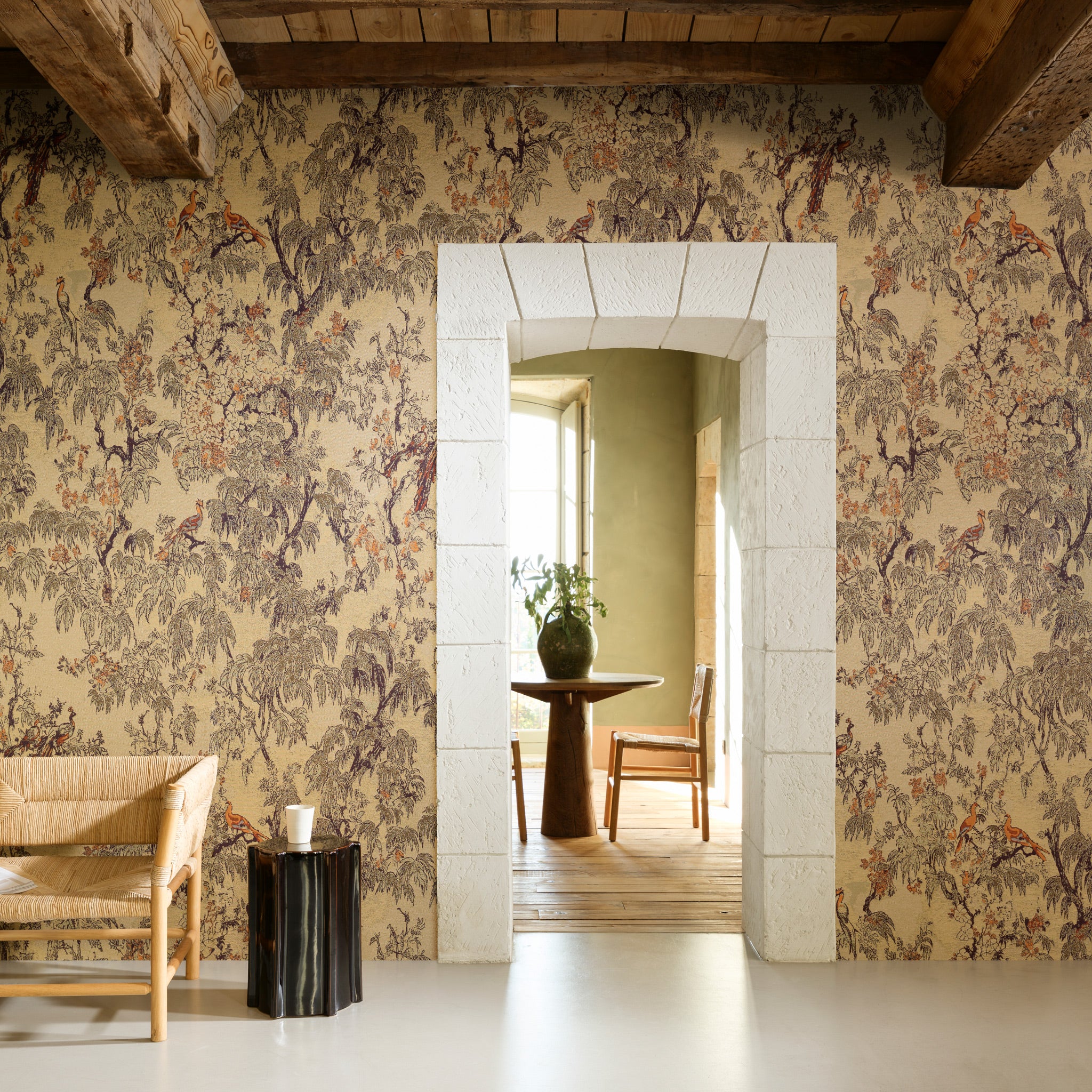 Room with floral wallpaper, wooden furniture, and a stone archway leading to another room.
