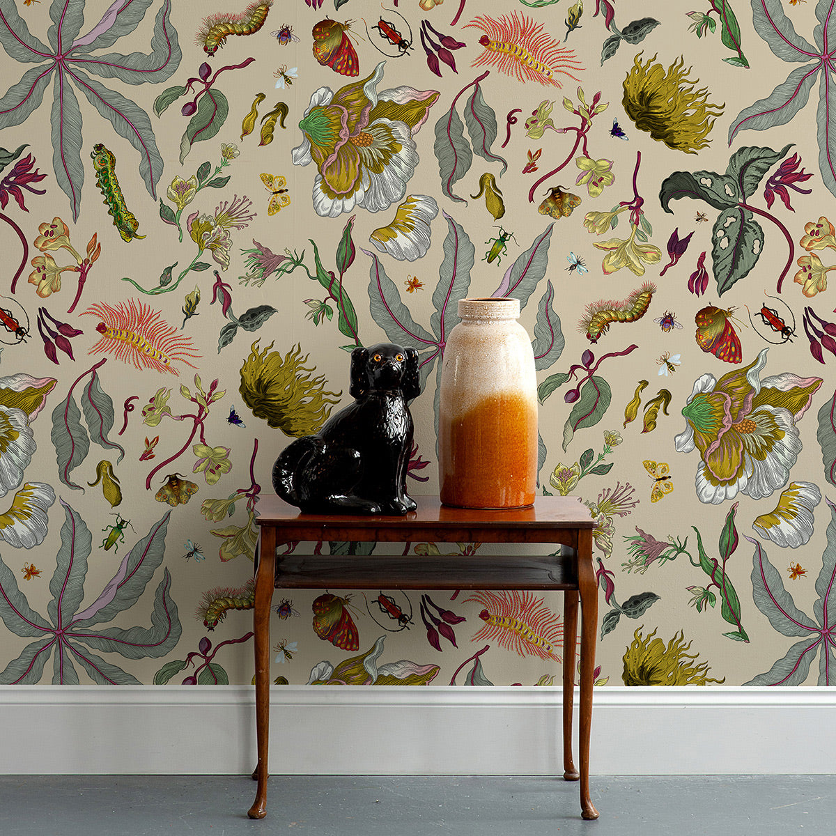 Decorative table with a vase and sculpture against a floral wallpapered wall.